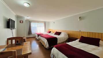 A hotel room with three beds, a desk, and a television.