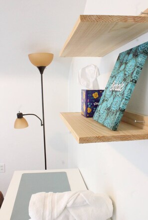 Una habitació amb una estant de fusta que conté una caixa de mocadors i un objecte decoratiu, una làmpada de peu i una tovallola sobre una taula.