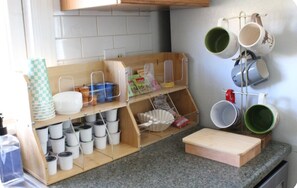 A kitchen with a wooden utensil rack holding pots and pans, a shelf with bowls and plates, and a cutting board on the counter. - Cozy 2-bedroom duplex in quaint Pittsburgh neighborhood (Pittsburgh)