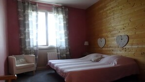 Une chambre à coucher avec un lit, une chaise, une fenêtre avec des rideaux, un radiateur et une horloge en forme de cœur accrochée au mur.
