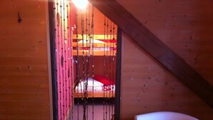 Une pièce avec un plafond en pente, un lit avec une literie rouge, un fauteuil blanc et un mur décoré de motifs en forme de cœur.