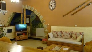 Un salon confortable avec un téléviseur, un canapé, une table basse et une arche décorative.