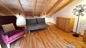 Une chambre à coucher aménagée dans un espace de type « loft », avec un plafond en bois, un canapé, un fauteuil, une commode et un lampadaire.
