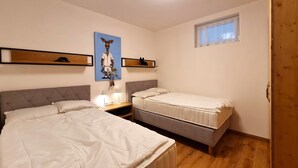 Une chambre avec deux lits, une table de chevet, une étagère murale avec un tableau, et une fenêtre.