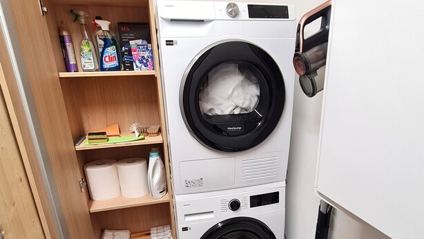 Une petite buanderie équipée d’un lave-linge et d’un sèche-linge à chargement frontal, d’une étagère pour les produits de nettoyage et d’un petit bac de rangement.