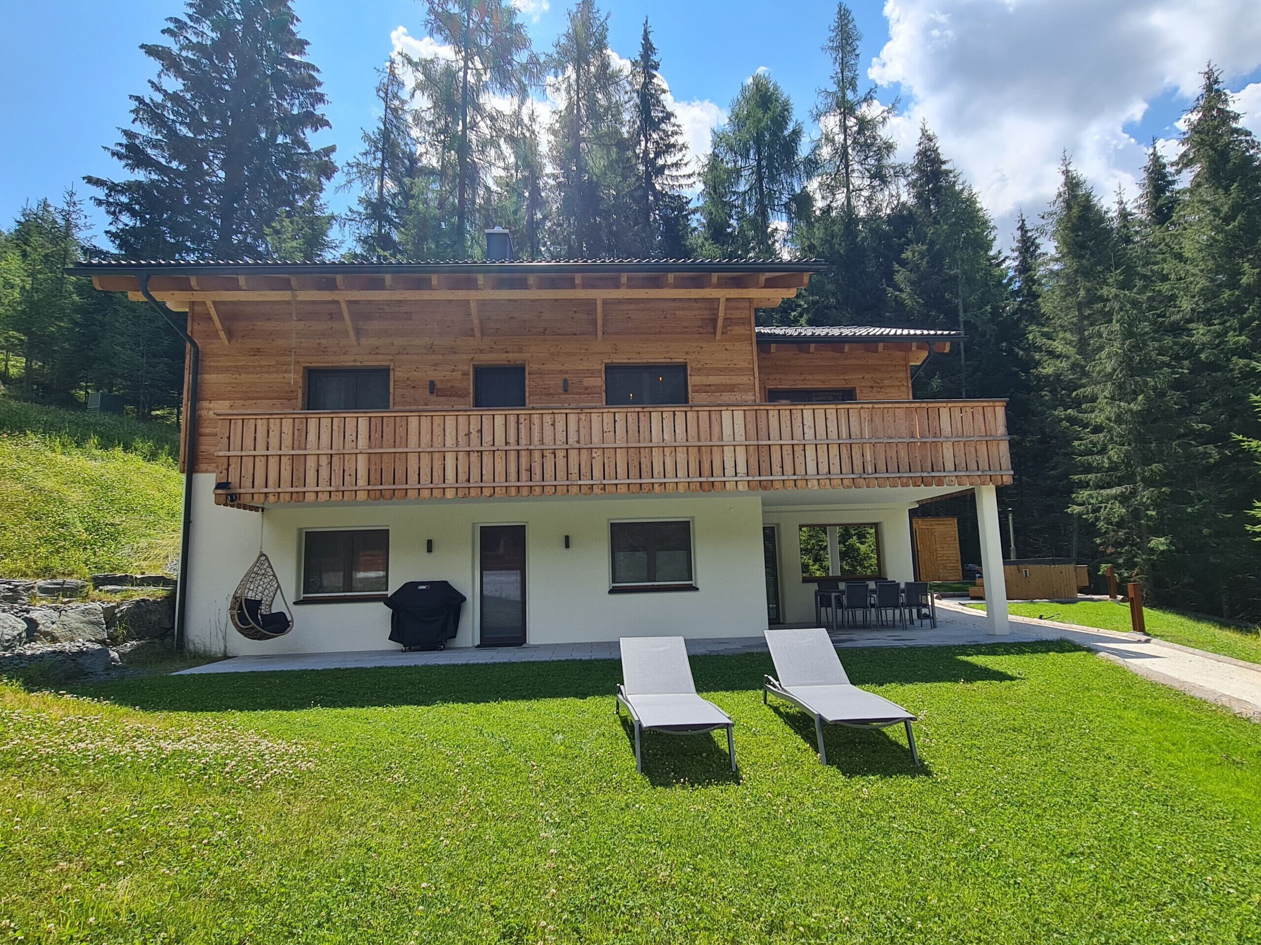 A two-story wooden house with a balcony, a covered patio, and a grassy lawn.