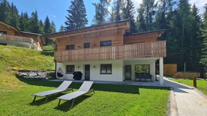 Un chalet en bois à deux étages, doté d’un balcon, d’une terrasse couverte et d’une pelouse où sont disposés des fauteuils de jardin.