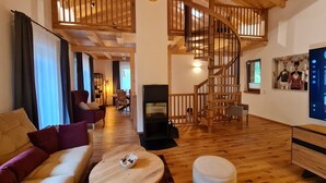Un vaste espace de vie agrémenté d’un escalier en bois, d’une cheminée et d’un téléviseur fixé au mur.
