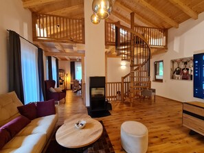 Amplia sala de estar con una escalera de madera, chimenea y televisor montado en la pared.