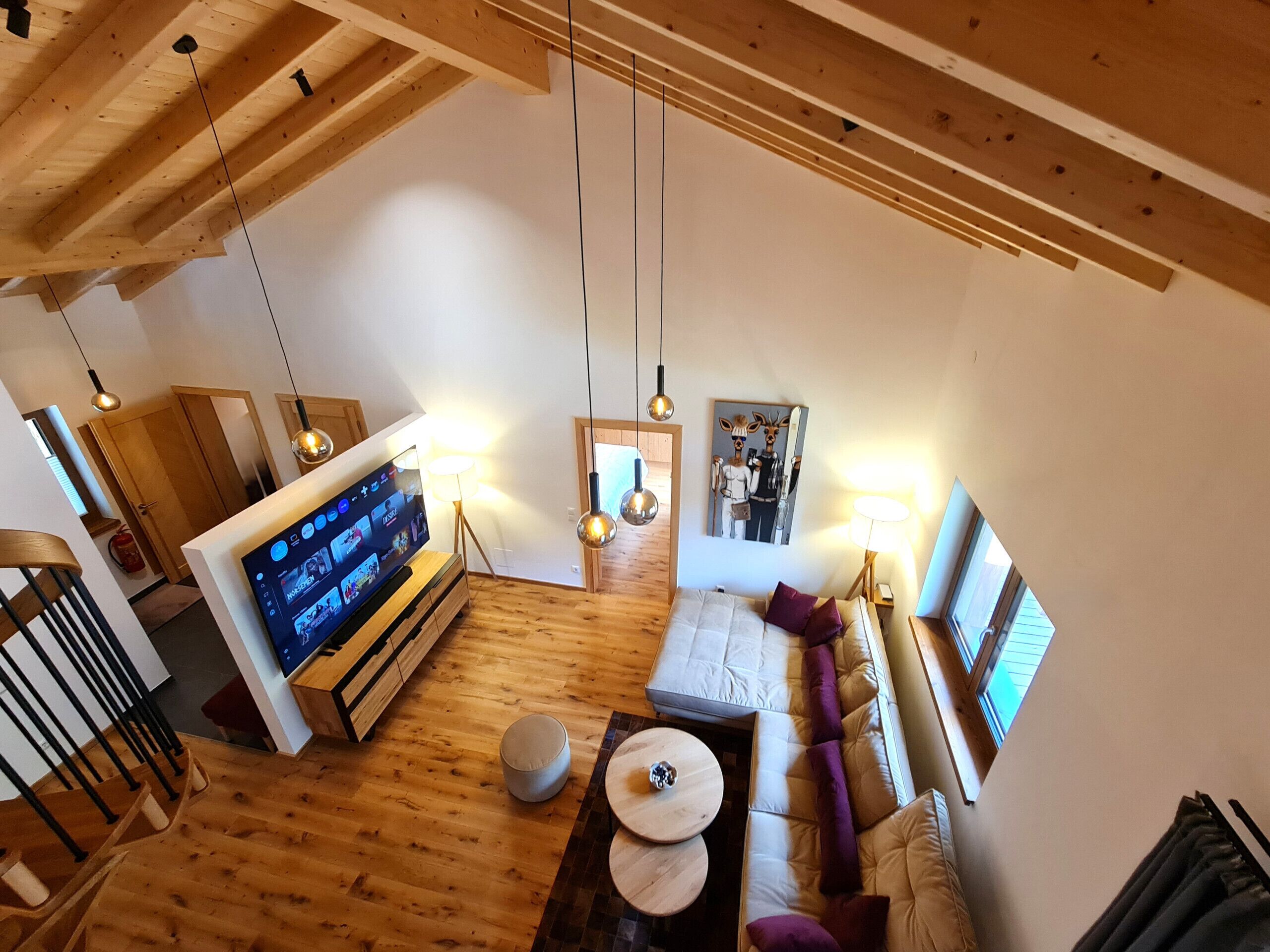 Een ruime woonkamer met houten vloer, een bank, een televisie en hanglampen.