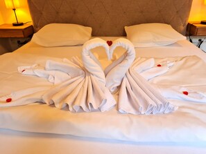 A bed with towels arranged in a heart shape, a headboard, and bedside lamps.