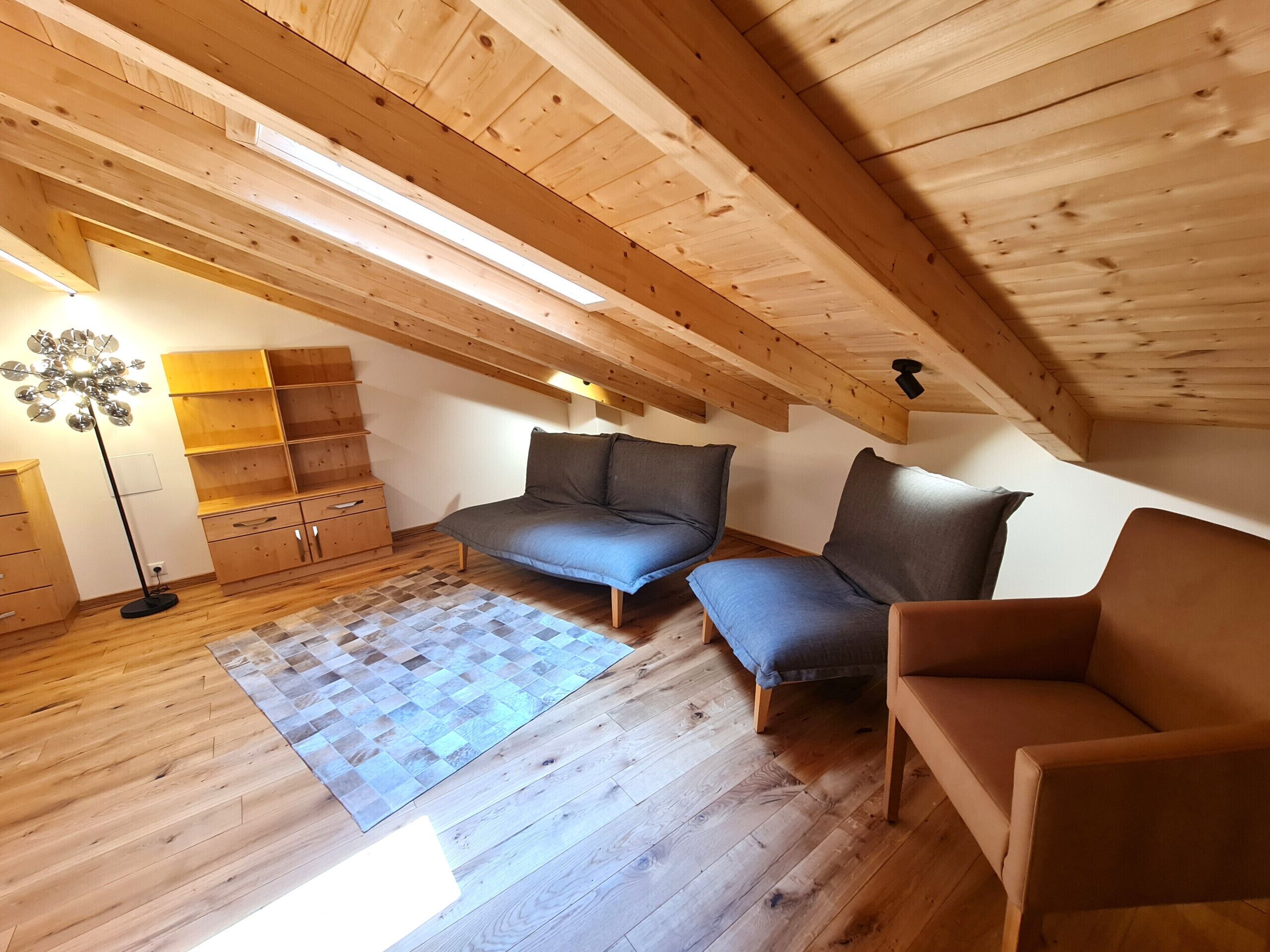 Une chambre à coucher de style loft avec un plafond en pente, un plancher en bois, un canapé, un fauteuil, une lampe sur pied et des étagères intégrées.
