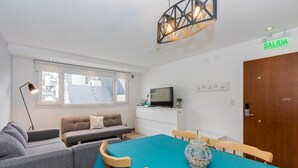A modern living room with a sofa, a dining table with chairs, a TV, and a door labeled 'SALIDA'. - Australis Apartamento Micro-centro (Ushuaia)