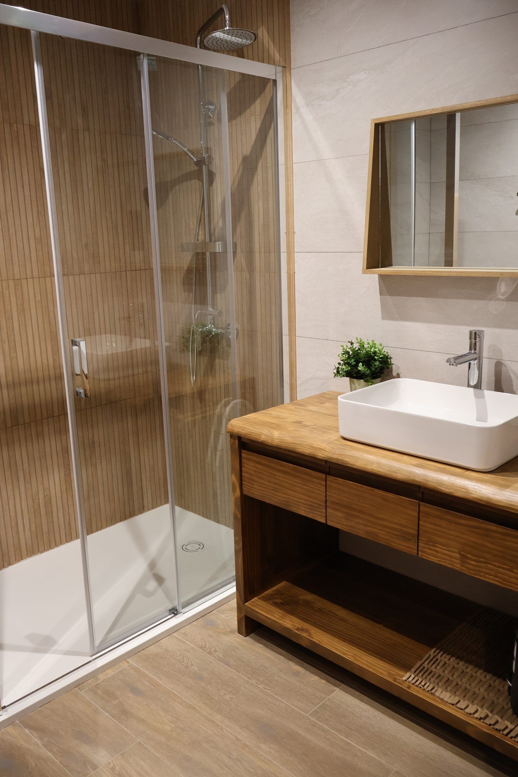 Un baño moderno con ducha envuelta en vidrio, tocador de madera y lavamanos blanco.