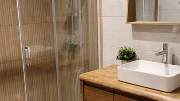 Un baño moderno con ducha envuelta en vidrio, tocador de madera y lavamanos blanco.