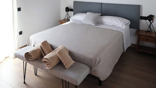 A bedroom with a large bed, a bench with towels, a nightstand, and a ceiling with exposed beams. - Country Villa Puerta del Gallo (Molina de Aragón–Alto Tajo) (Molina de Aragón)