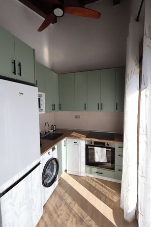 A compact kitchen with a washing machine, a built-in oven, and a ceiling fan.