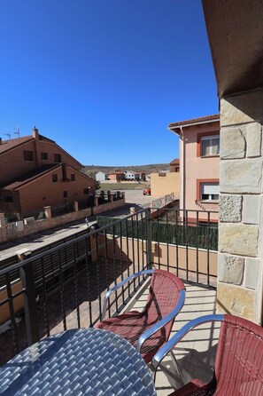 A balcony with metal chairs and a table, overlooking a residential area with houses and a clear blue sky.