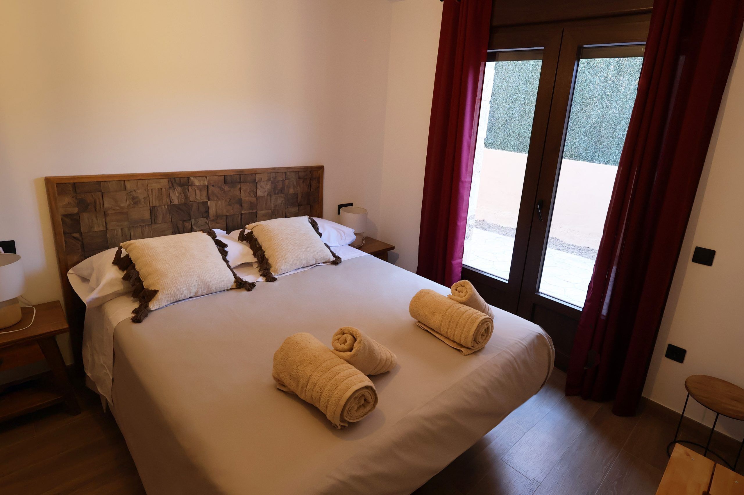Habitación de hotel con una cama grande, dos almohadas, una mesita de noche, una lámpara y vistas a través de un ventanal.