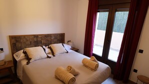 A hotel room with a large bed, two pillows, a bedside table, a lamp, and a view through a glass door. - Country Villa Puerta del Gallo (Molina de Aragón–Alto Tajo) (Molina de Aragón)