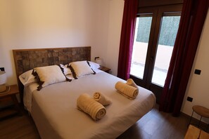Habitación de hotel con una cama grande, dos almohadas, una mesita de noche, una lámpara y vistas a través de un ventanal.