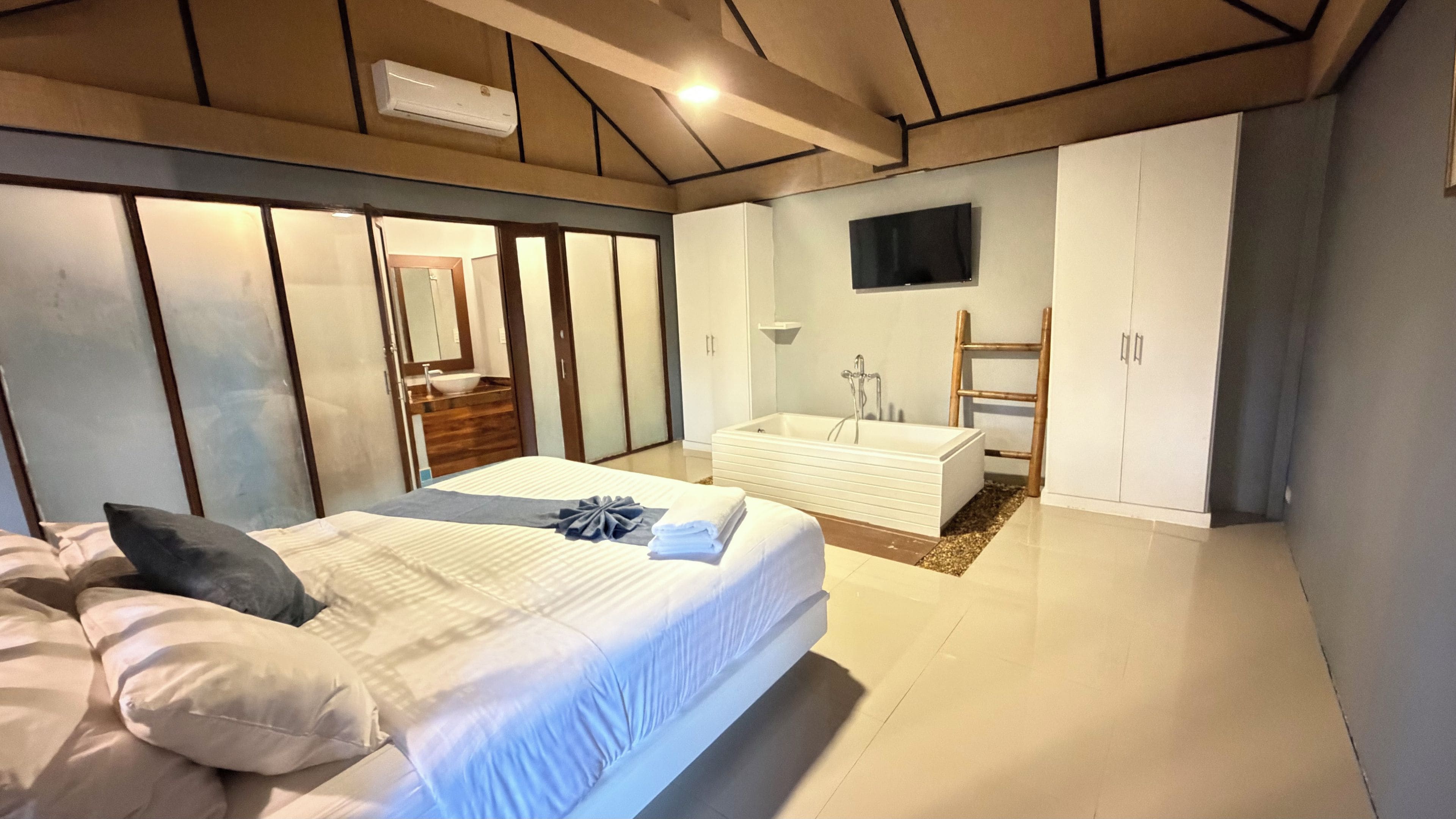 A bedroom with a bed, a bathroom with a bathtub, and a TV mounted on the wall.