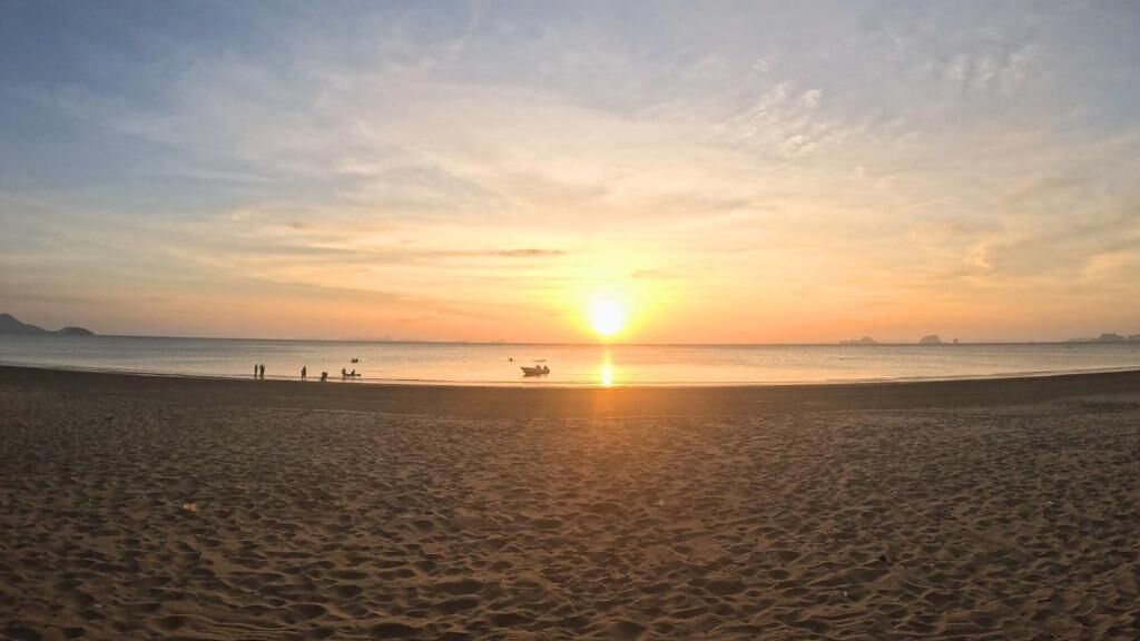 Una playa al atardecer, mar tranquilo y algunas personas a lo lejos.