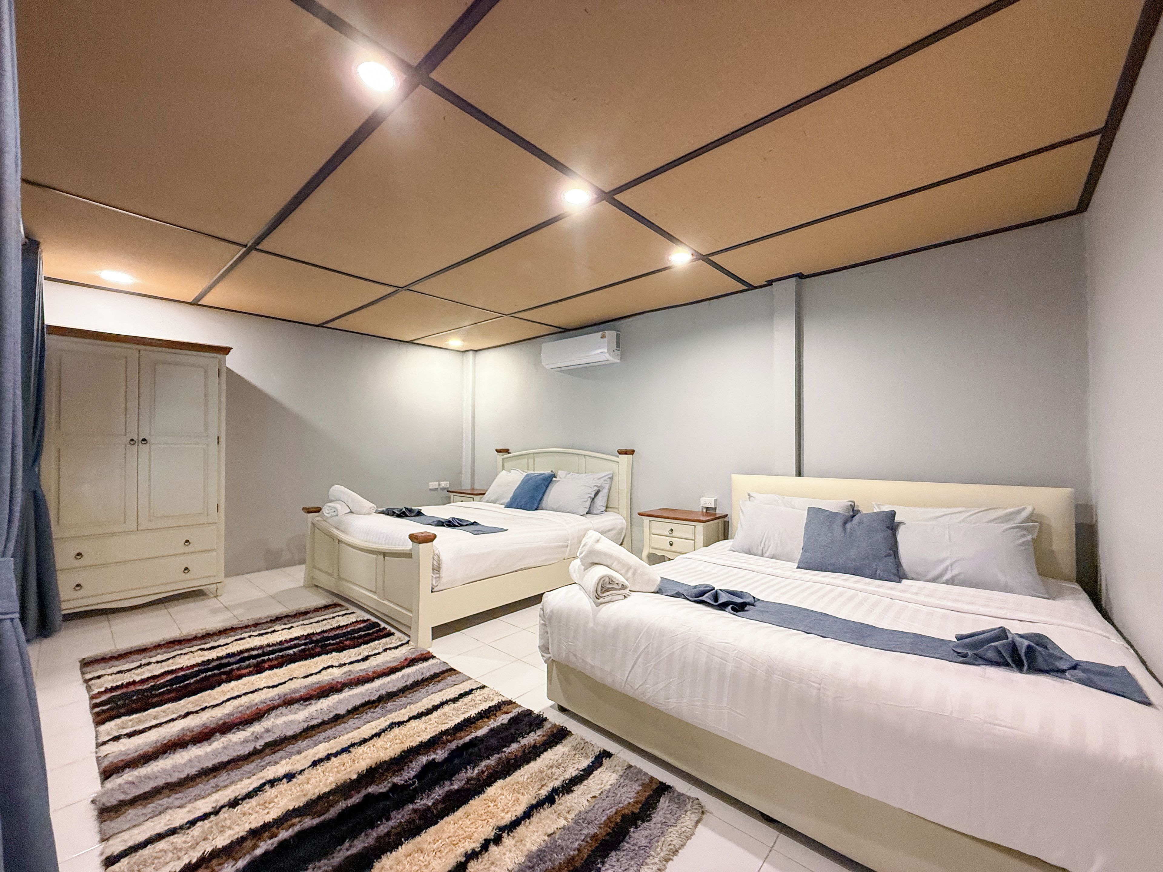 Une chambre d’hôtel avec deux lits, une armoire, une table de chevet et une lampe sur pied.