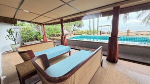 Un área de estar al aire libre techada con piscina, mobiliario de madera y vistas al mar.