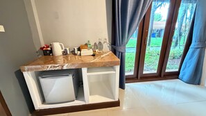 Una encimera de cocina con una cafetera, tazas y un cubo de basura.