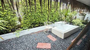 A spa area with a bathtub, a chair, and a small table, surrounded by greenery and a gravel floor.