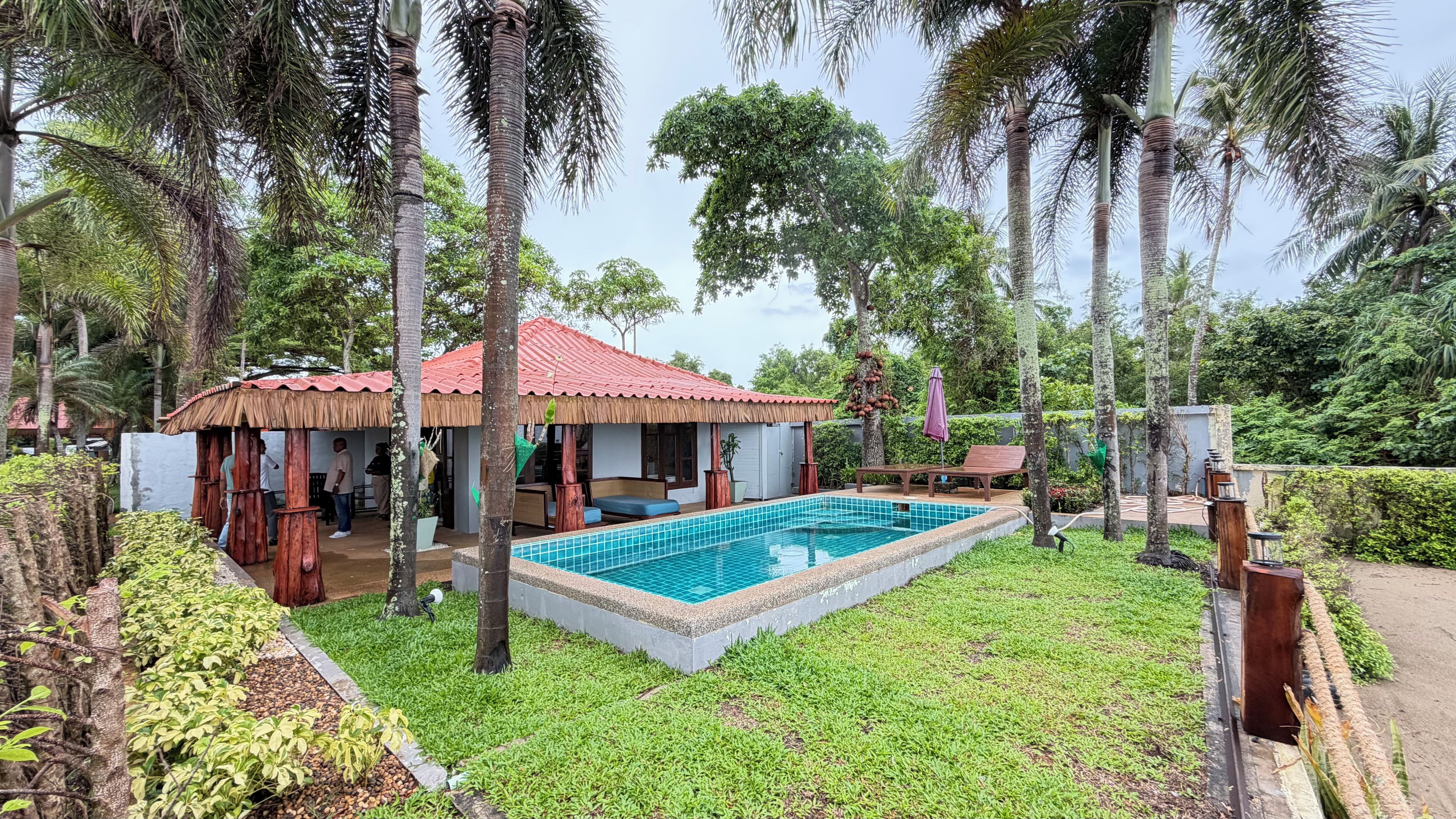 A pool area with a tiled pool, lounge chairs, and a thatched-roof structure.