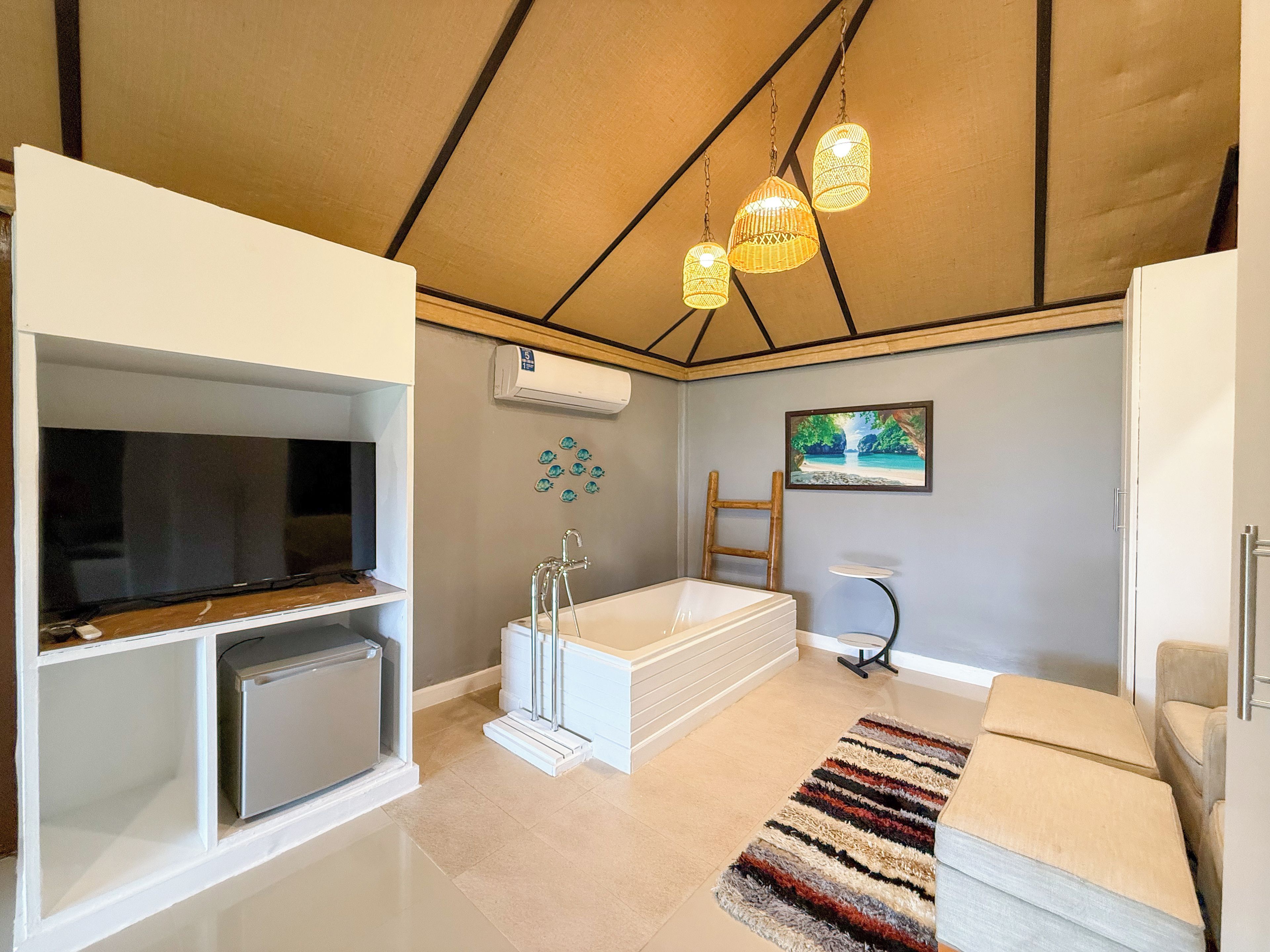 A modern bathroom with a bathtub, a shower, and a toilet. There is a television on a stand and a painting on the wall.