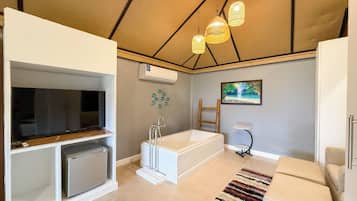 A modern bathroom with a bathtub, a shower, and a toilet. There is a television on a stand and a painting on the wall.
