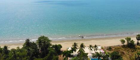 Vista de la playa con cielo despejado, piscina y un barco en el agua.