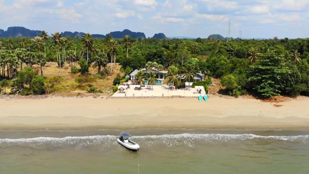 A beach with a house and palm trees in the background.