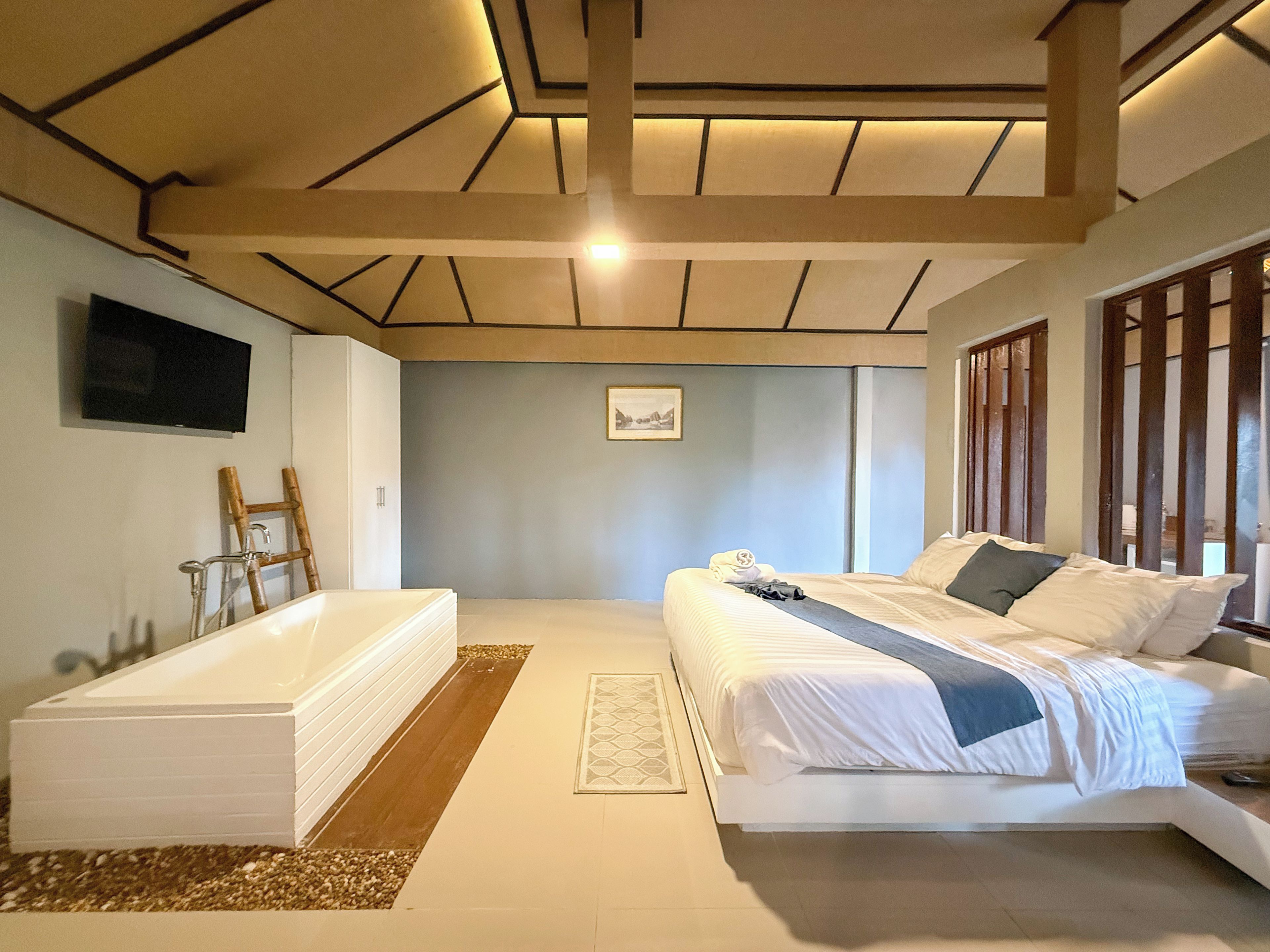 A bedroom with a large bed, a built-in bathtub, and a television on the wall.