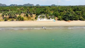 Una playa con un bote, una casa y vegetación densa al fondo.