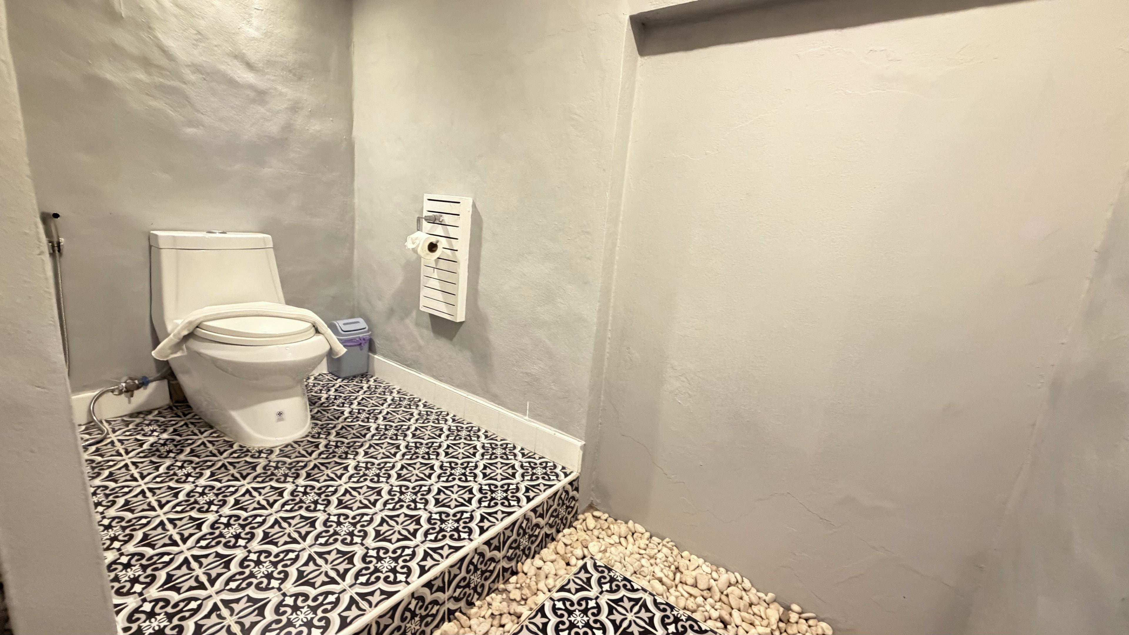 Une salle de bain équipée de toilettes, d’une poubelle et d’un porte-rouleau de papier toilette fixé au mur.