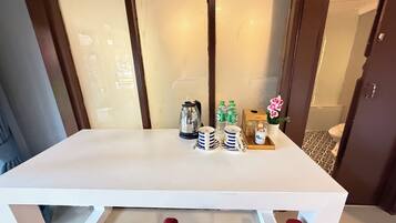 A hotel room with a white table set with a kettle, water bottles, cups, and a small plant.