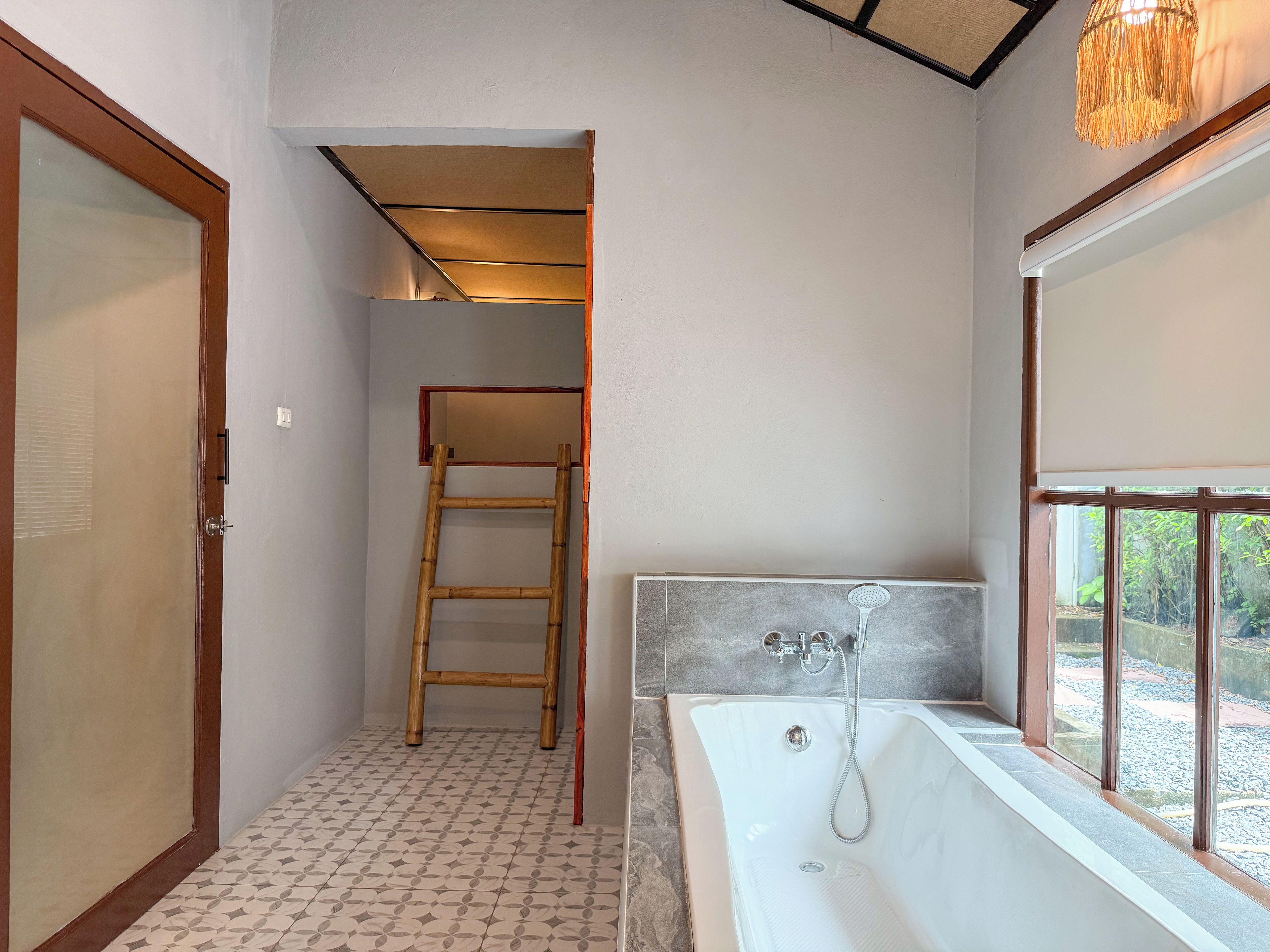 A bathroom with a bathtub, a shower, a wooden ladder, and a window with a view.