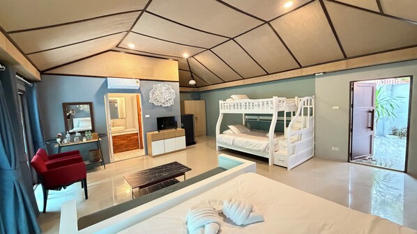A modern hotel room with a bunk bed, a desk with a chair, a vanity with a mirror, and a large bed with a neatly folded towel.