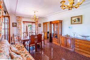A well-lit dining area with a chandelier, wooden furniture, and a view through a glass door. - Cubo's Paraje Galiano Rural House / Private pool / BBQ / Free Wi-Fi (Guaro)