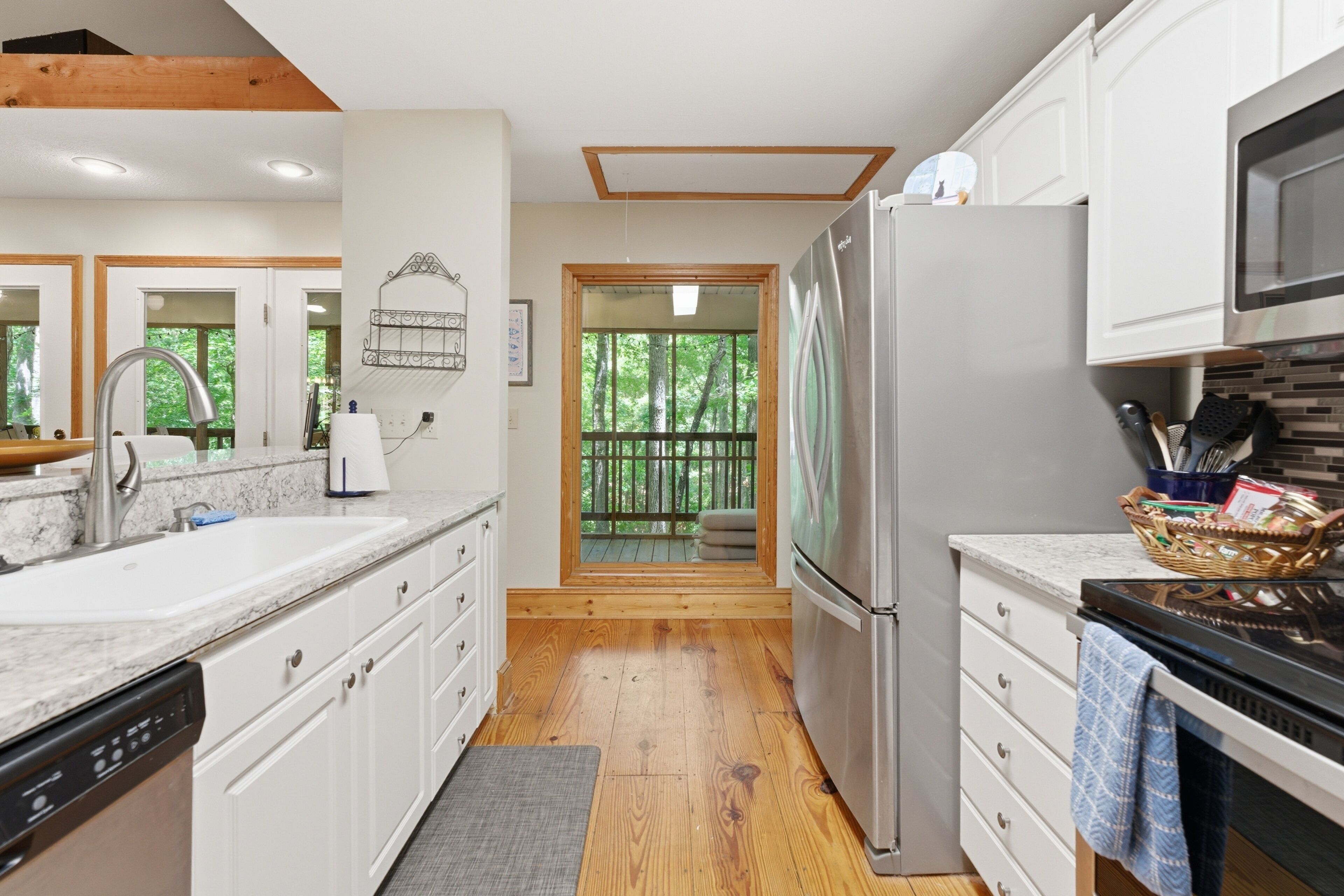 A modern kitchen with white cabinetry, a stainless steel refrigerator, and a wooden deck visible through a glass door.