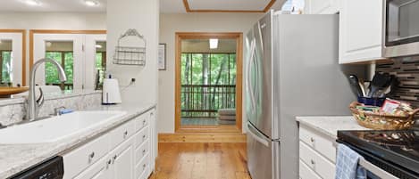 A modern kitchen with white cabinetry, a stainless steel refrigerator, and a wooden deck visible through a glass door.
