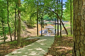 A concrete pathway leading to a covered dock area with a view of a lake and buildings in the distance. - Lake Hartwell Home w/Dock, Hot Tub, Foosball, Ping Pong, Mini Golf & BBQ! (Lavonia)