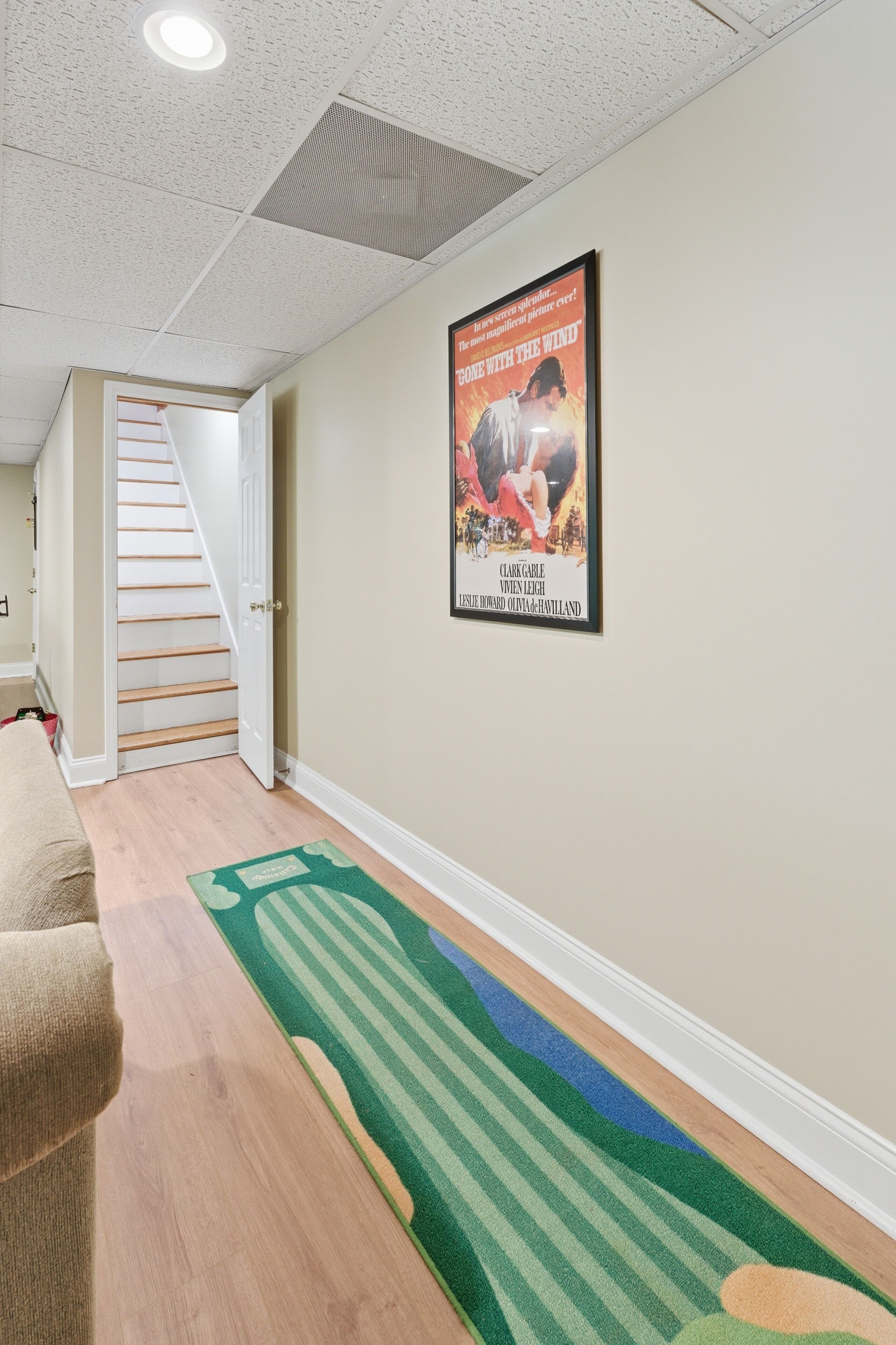 Un couloir avec un tapis, une affiche accrochée au mur et un escalier.