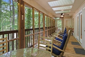 A covered outdoor seating area with wooden railings, a glass table, and blue cushioned chairs. - Lake Hartwell Home w/Dock, Hot Tub, Foosball, Ping Pong, Mini Golf & BBQ! (Lavonia)