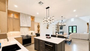 A modern kitchen with a central island, built-in appliances, and a dining area with a sofa and chairs. - Taylor Marae House - Close to all of Waco's Attractions! (Waco)