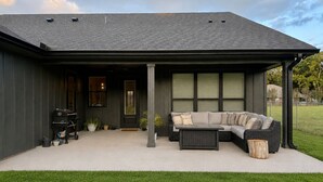 Una casa moderna amb un porxo cobert, un sofà modular i una barbacoa a l'exterior.